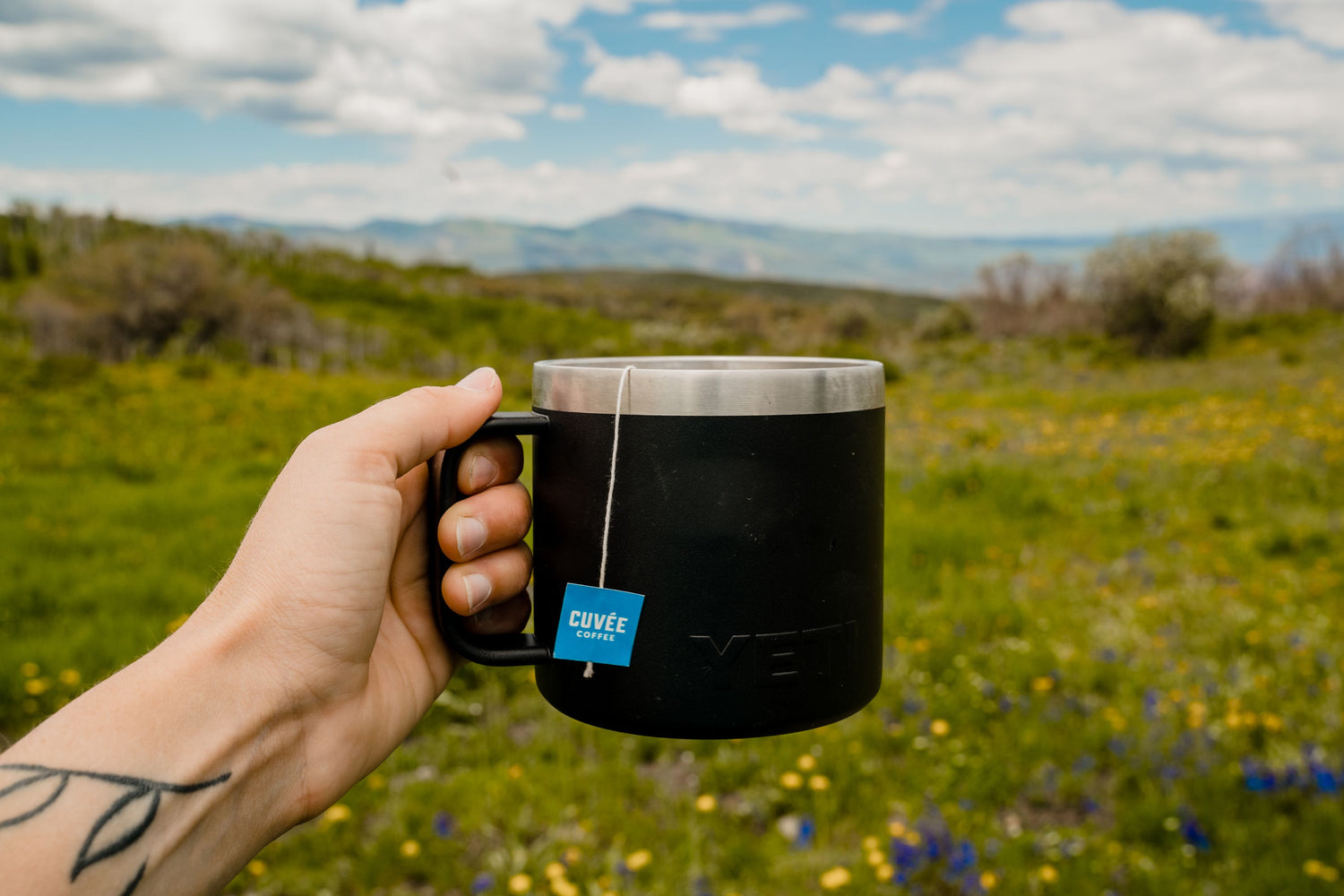 Hand holding a cup of Cuvée coffee in a serene outdoor