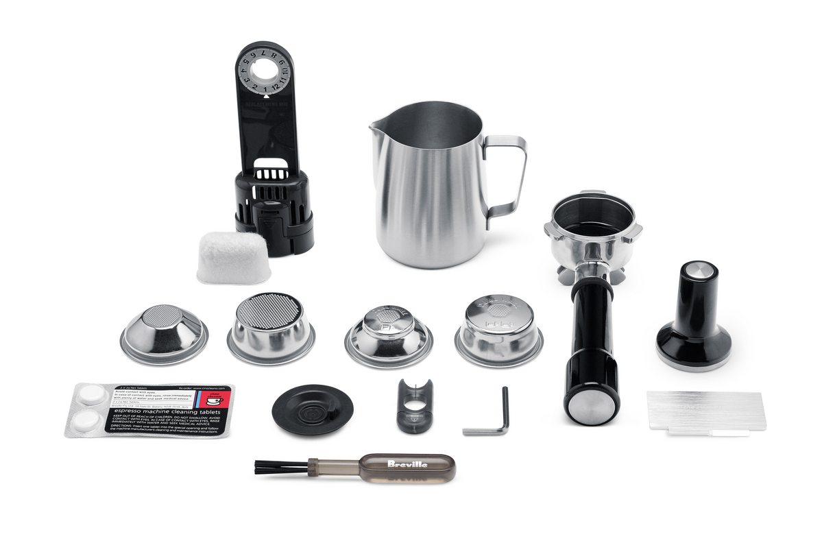 Accessories for the Breville - The Barista Express™, including a milk frothing pitcher, filter baskets, portafilter, tamper, cleaning brush, measuring spoon, and cleaning tablets arranged on a white background.