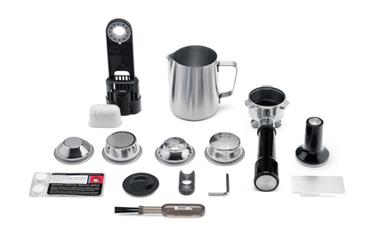 Accessories for the Breville - The Barista Express™, including a milk frothing pitcher, filter baskets, portafilter, tamper, cleaning brush, measuring spoon, and cleaning tablets arranged on a white background.