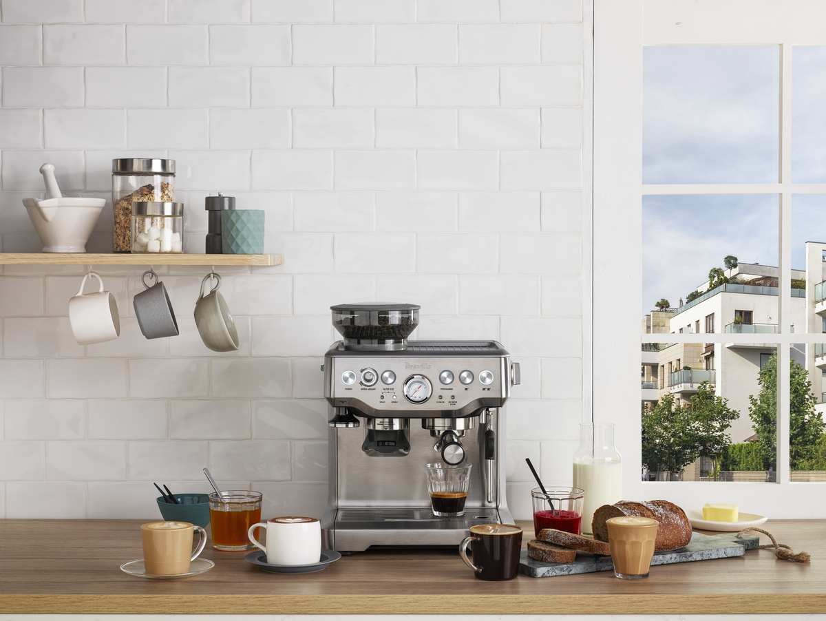 A Breville - The Barista Express™ espresso machine with a built-in grinder sits on the counter, surrounded by coffee cups.